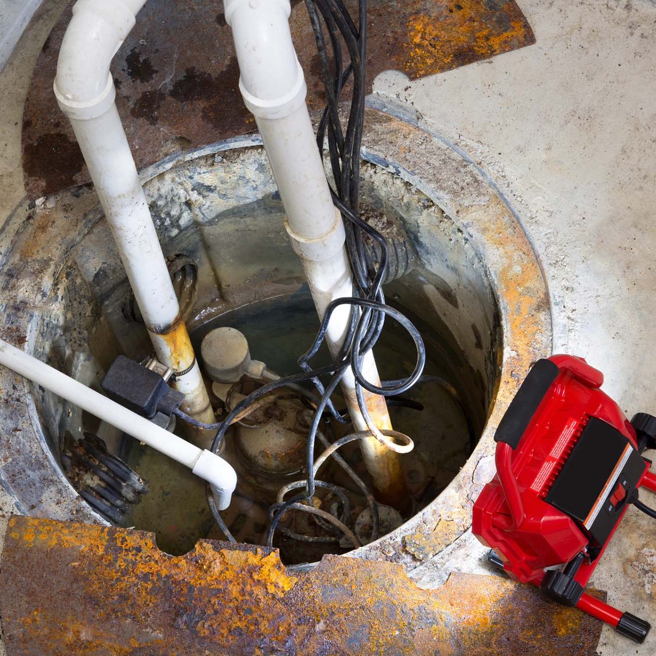 Repairing a sump pump in a basement with a red LED light illuminating the pit and pipe work for draining ground water