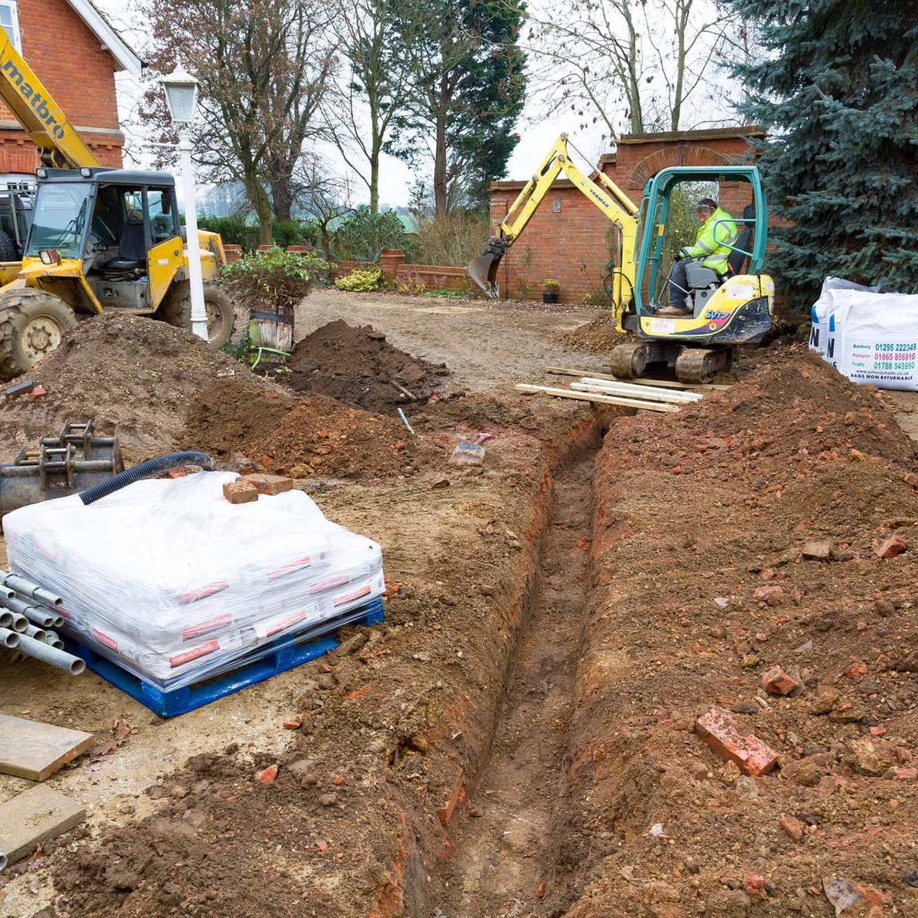 Digging a trench for drains, UK building site. BUCKINGHAM, UK - December 02, 2016. Digger driver, digging a trench for drains on a UK building site